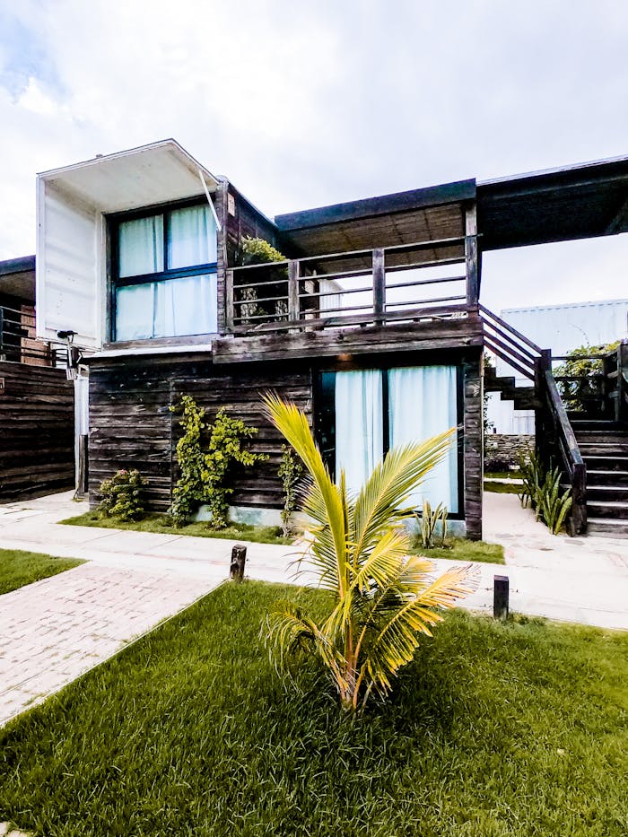 Contemporary two-story wooden house with lush greenery and palm plants.